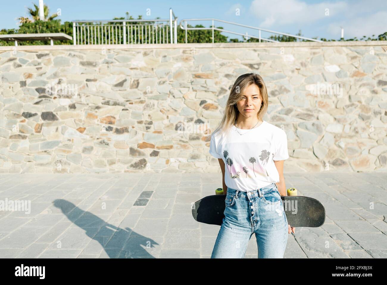 Donna bionda con skateboard durante la giornata di sole nel parco Foto Stock