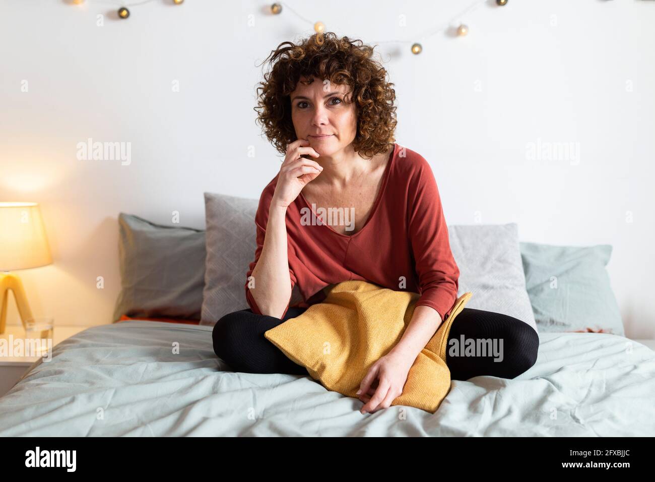 Donna matura seduta sul letto a casa Foto Stock