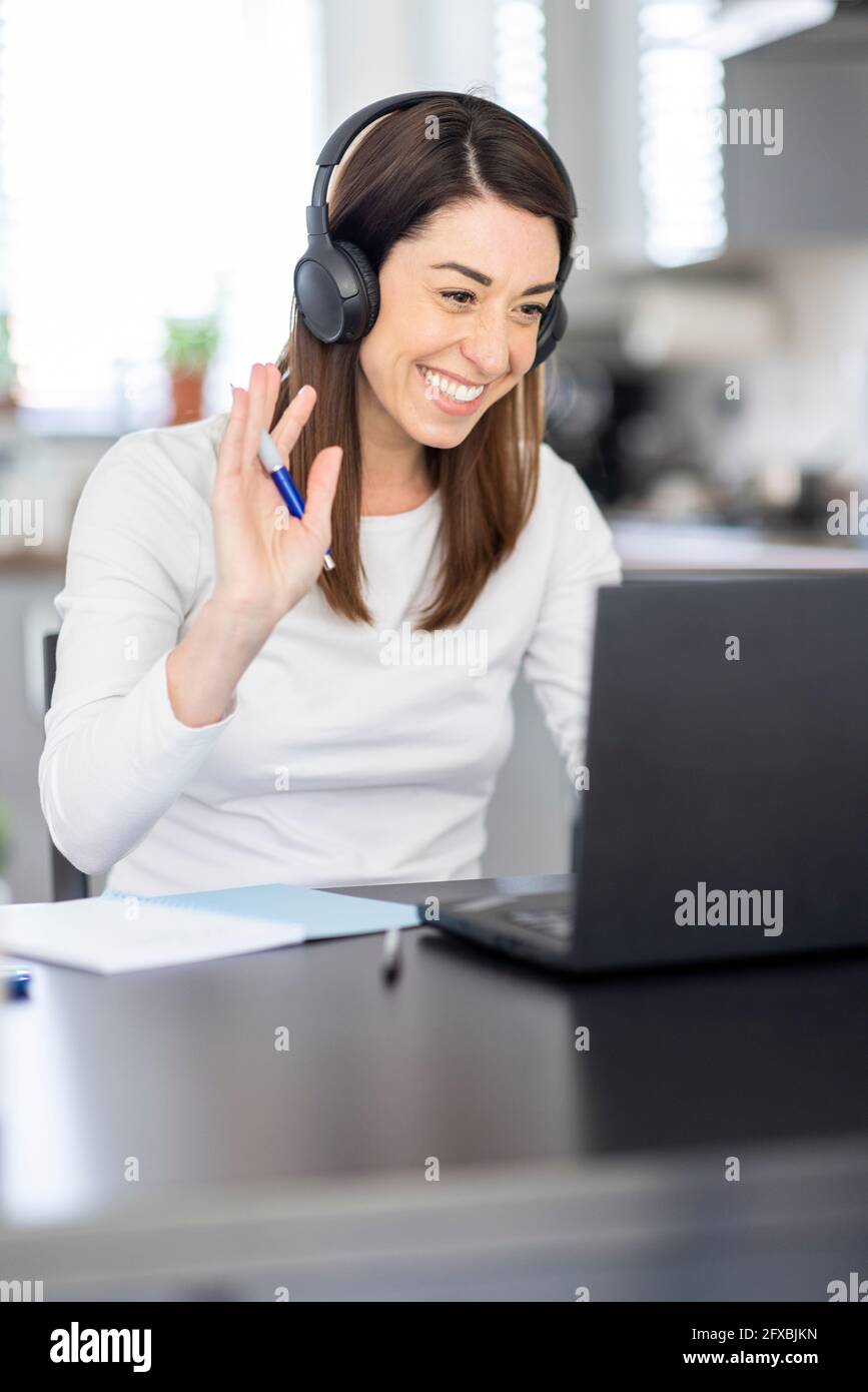 Sorridente donna professionista che vacilla durante la videoconferenza attraverso il computer portatile a casa Foto Stock
