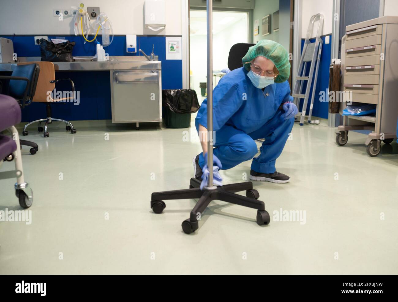 Donna dal servizio di pulizia di un ospedale che si accovacciano la pulizia un bastone di farmaco endovenoso per il farmaco intravenoso portatile da il previo Foto Stock
