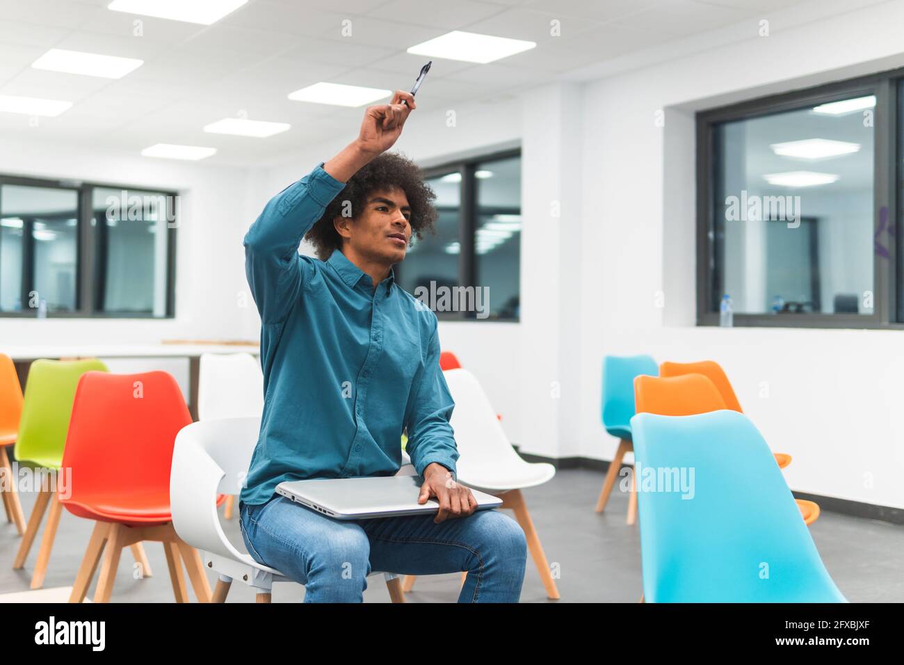 Uomo d'affari che alza la mano mentre si siede con un computer portatile nella sala della classe di istruzione Foto Stock