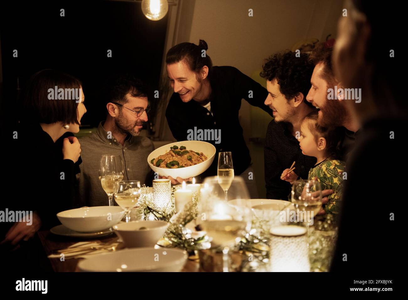 Sorridendo uomini e donne che guardano la pasta tenuta dall'uomo maturo in cucina Foto Stock