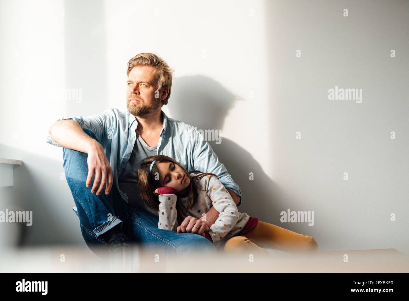 Figlia che riposa sul grembo del padre davanti al muro a casa Foto Stock