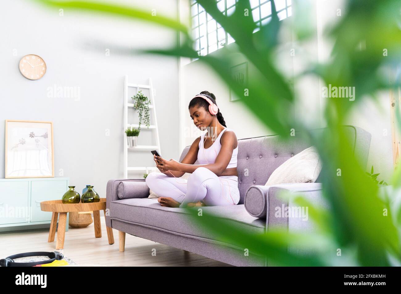 Giovane donna in abbigliamento sportivo che usa lo smartphone sul divano di casa Foto Stock