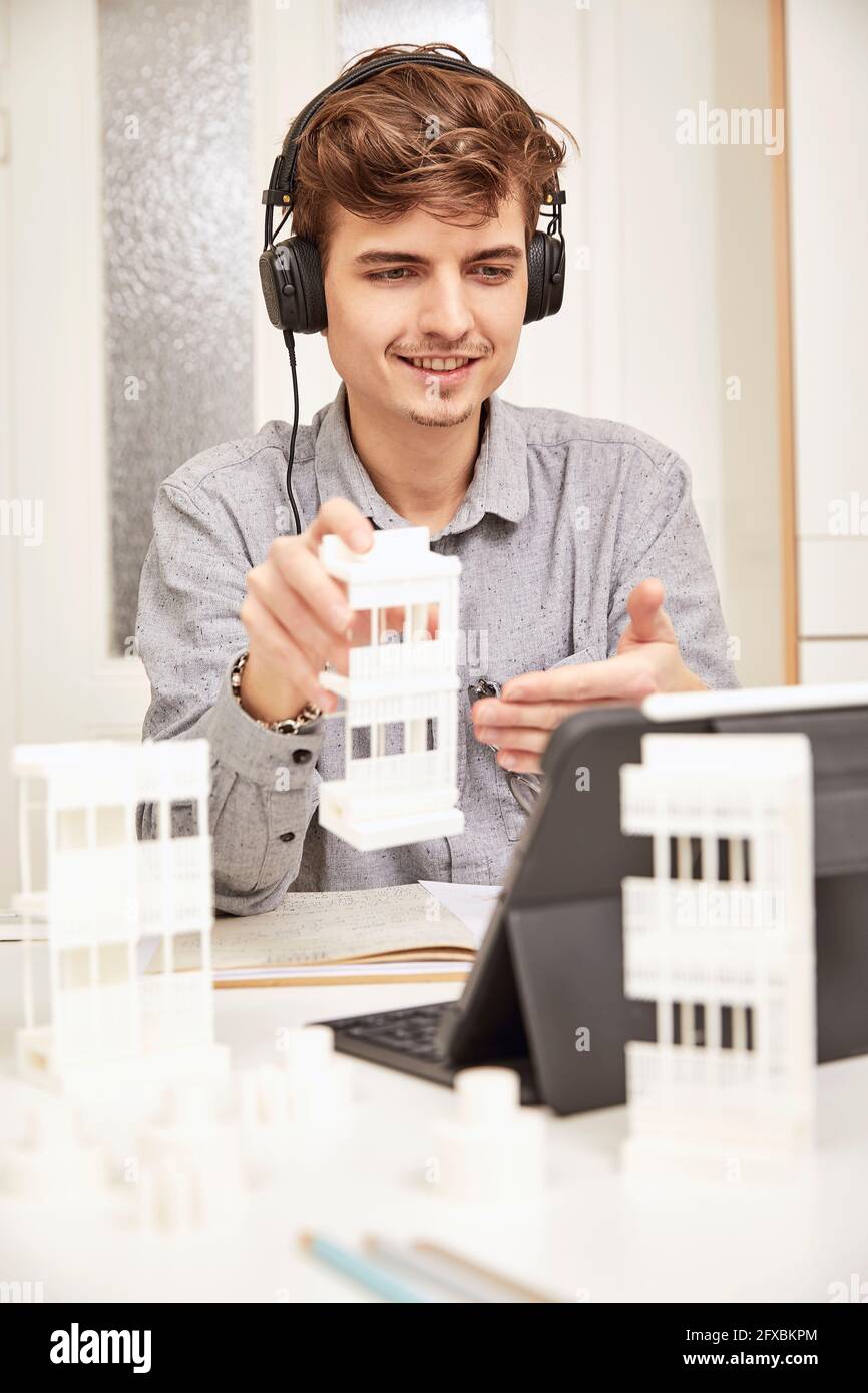 Sorridente architetto maschile che spiega il modello architettonico durante la videoconferenza in ufficio Foto Stock