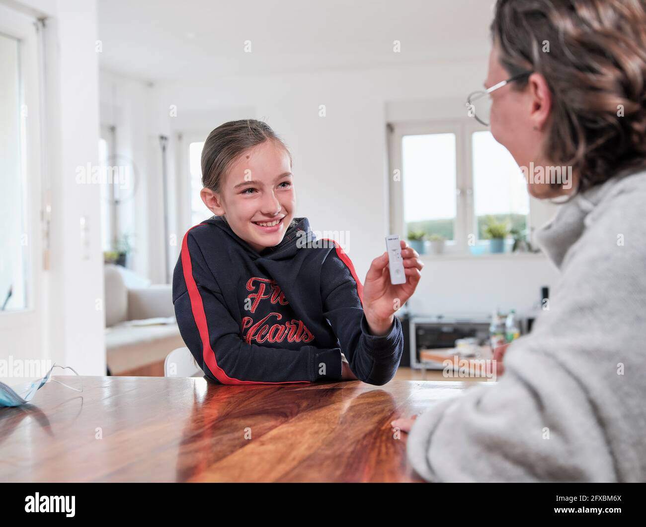 Sorridente ragazza che mostra negativo COVID-19 test per la madre a casa Foto Stock