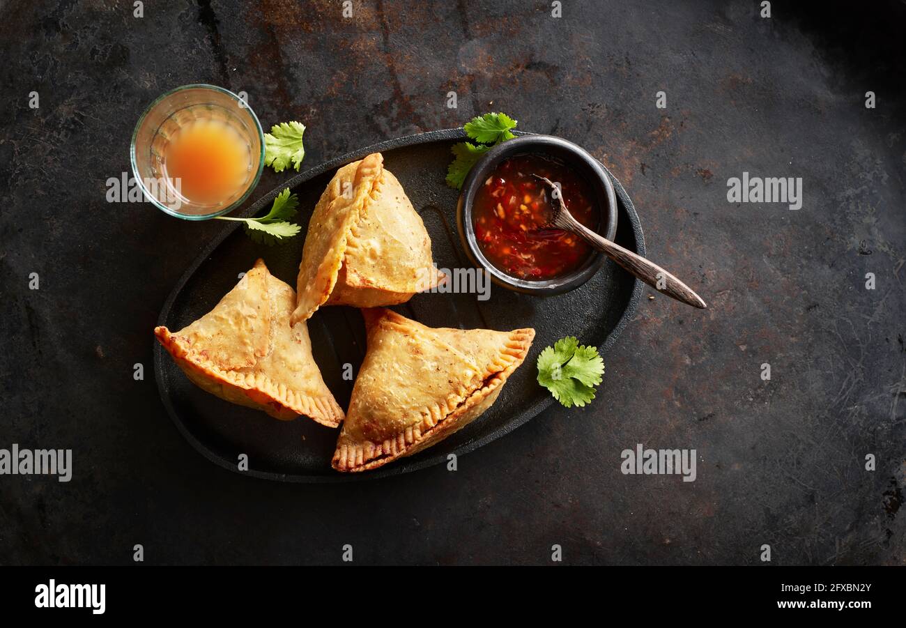 Vassoio con gnocchi di samosa, ciotola di salsa al peperoncino e bicchiere di tè chai Foto Stock