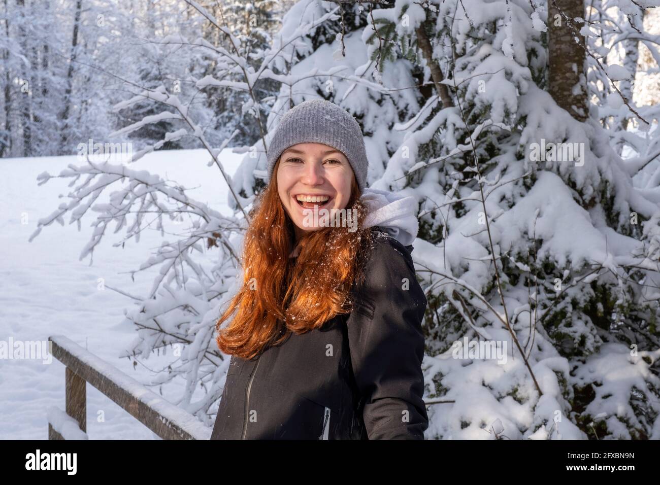 Donna felice con capelli rossi di fronte all'albero coperto di neve durante l'inverno Foto Stock