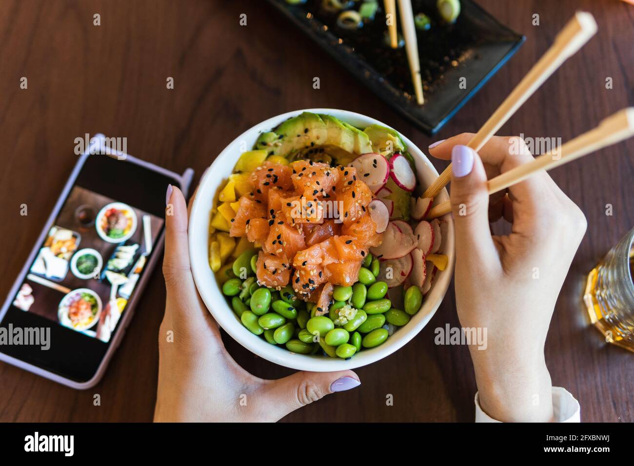 Giovane donna che ha una ciotola di poke con i chopsticks sul tavolo al bar Foto Stock