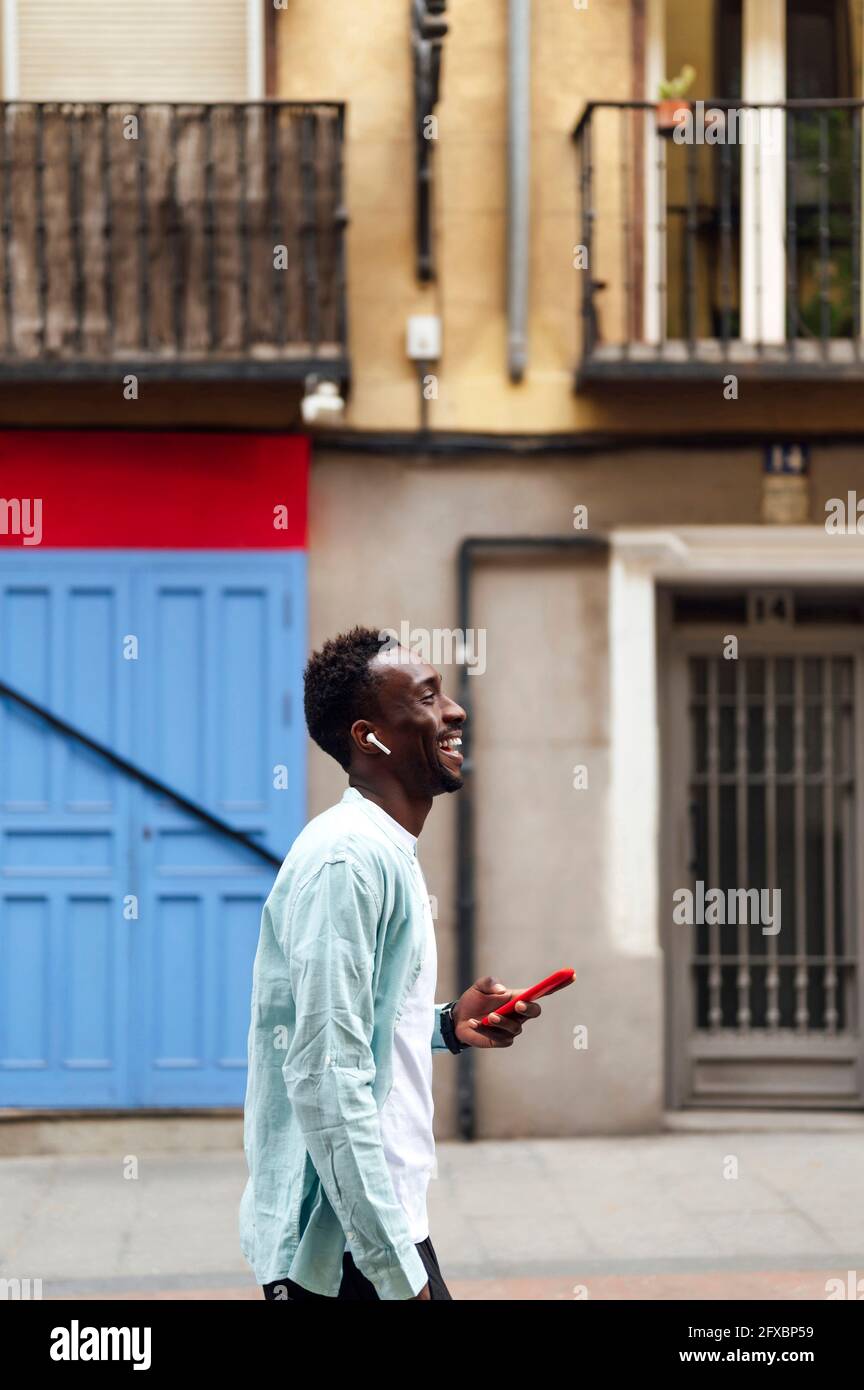 Giovane uomo con smartphone e cuffie intrauricolari per strada Foto Stock