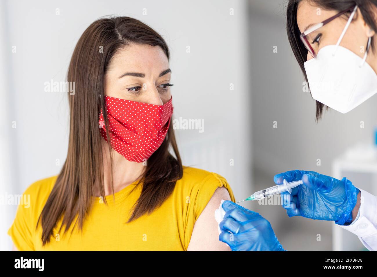 Donna che indossa una maschera protettiva per il viso guardando il medico femminile che dà il vaccino durante COVID-19 Foto Stock
