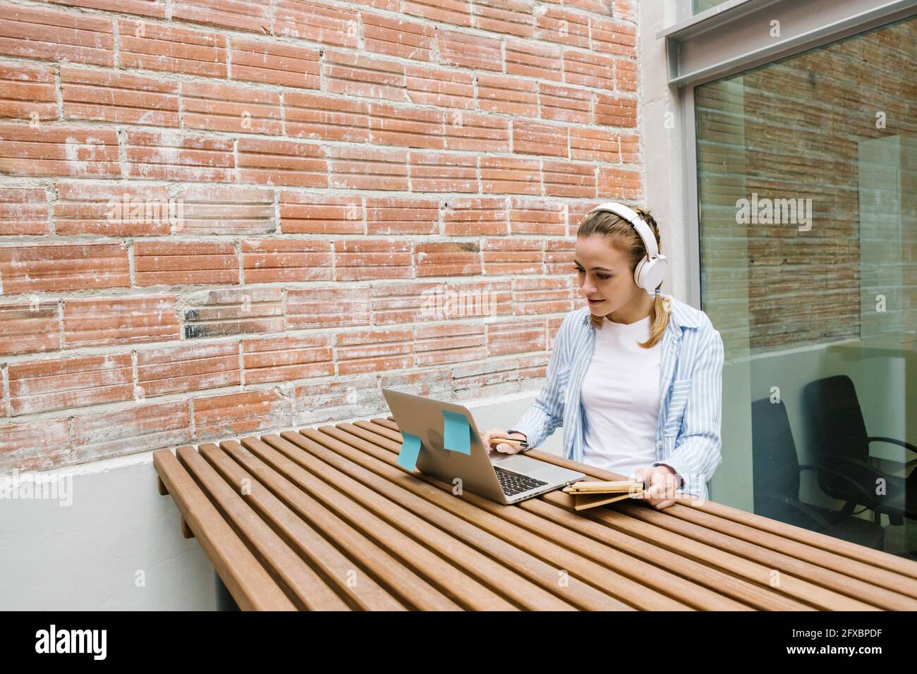 Donna professionista che indossa le cuffie che partecipa alla videochiamata sul computer portatile presso la caffetteria Foto Stock