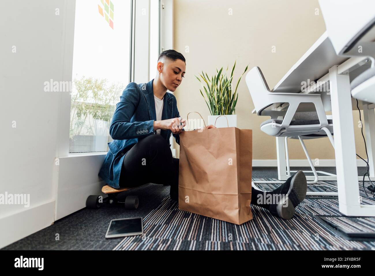Donna d'affari che guarda la borsa di carta mentre si siede in ufficio Foto Stock