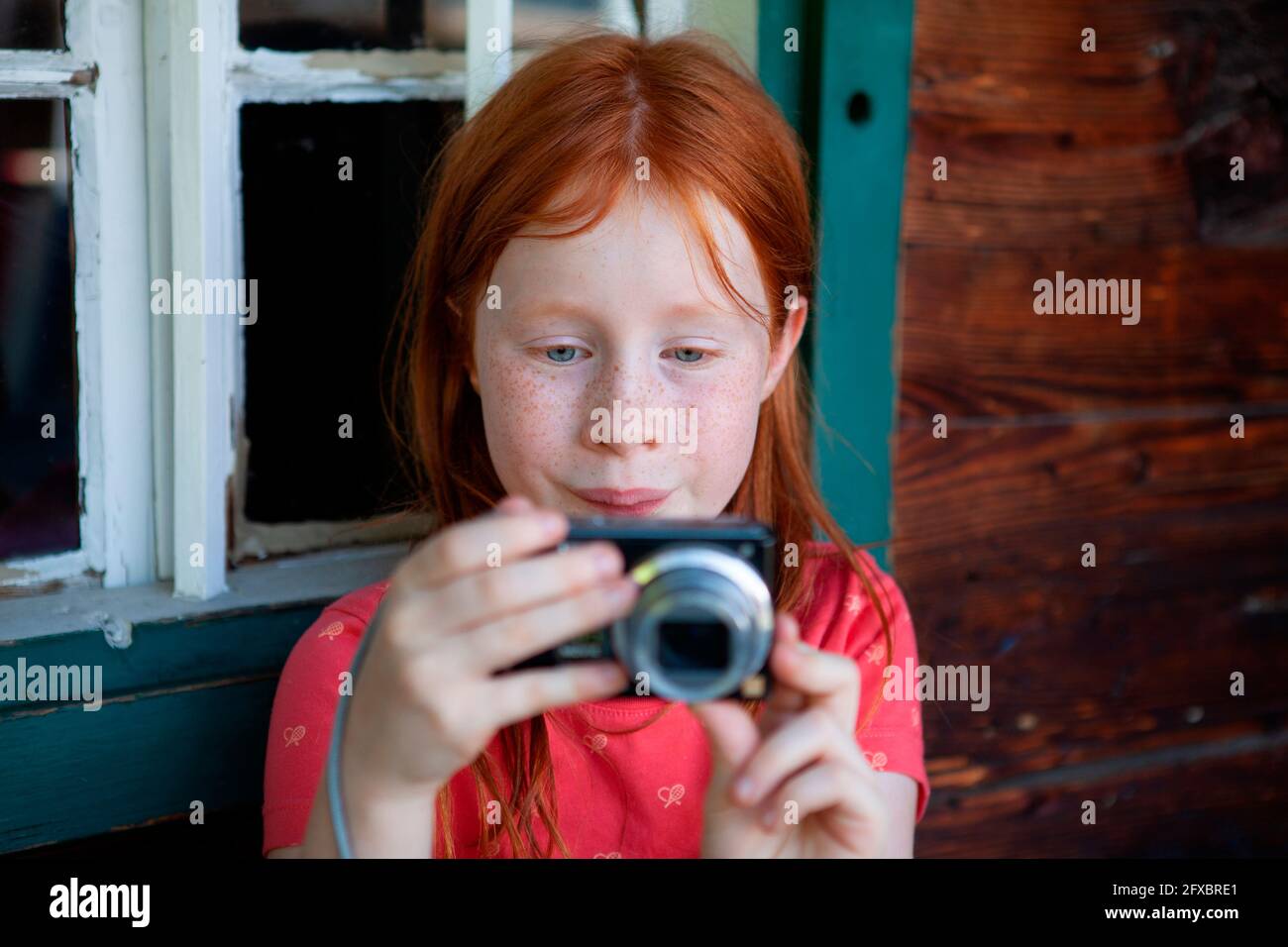 Ragazza rossa fotografando attraverso la macchina fotografica dalla finestra Foto Stock