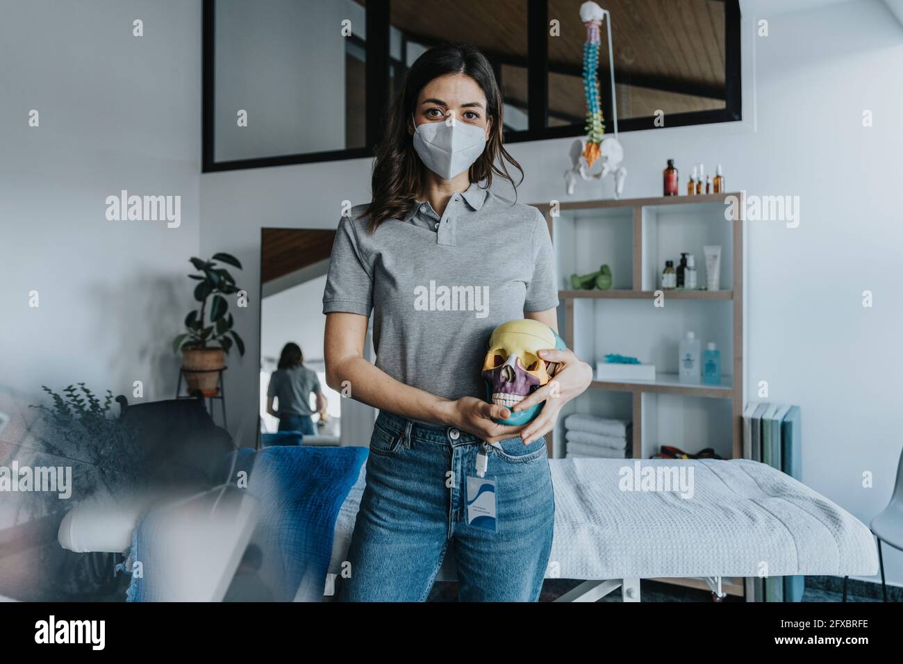 Fisioterapista femminile che indossa una maschera protettiva che tiene in pratica il modello del cranio Foto Stock
