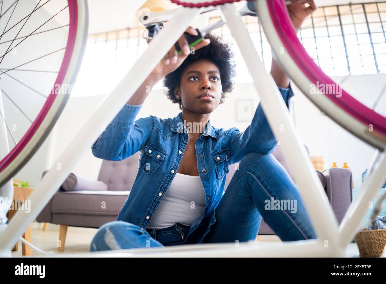 Donna afro che tiene l'attrezzo di lavoro mentre ripara la bicicletta a casa Foto Stock