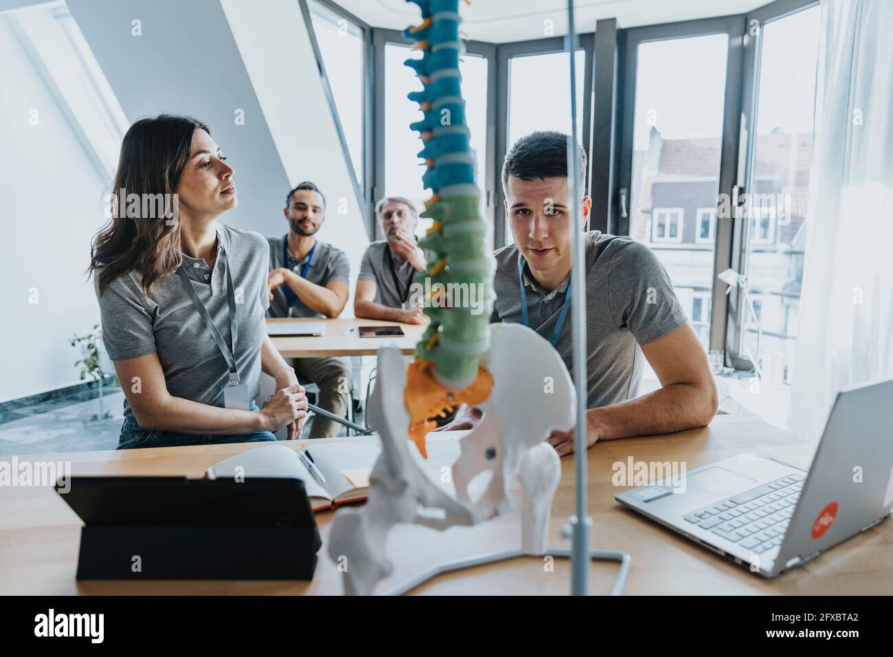 Tirocinante maschile che guarda il modello della colonna vertebrale da parte di una collega femminile in classe di formazione Foto Stock