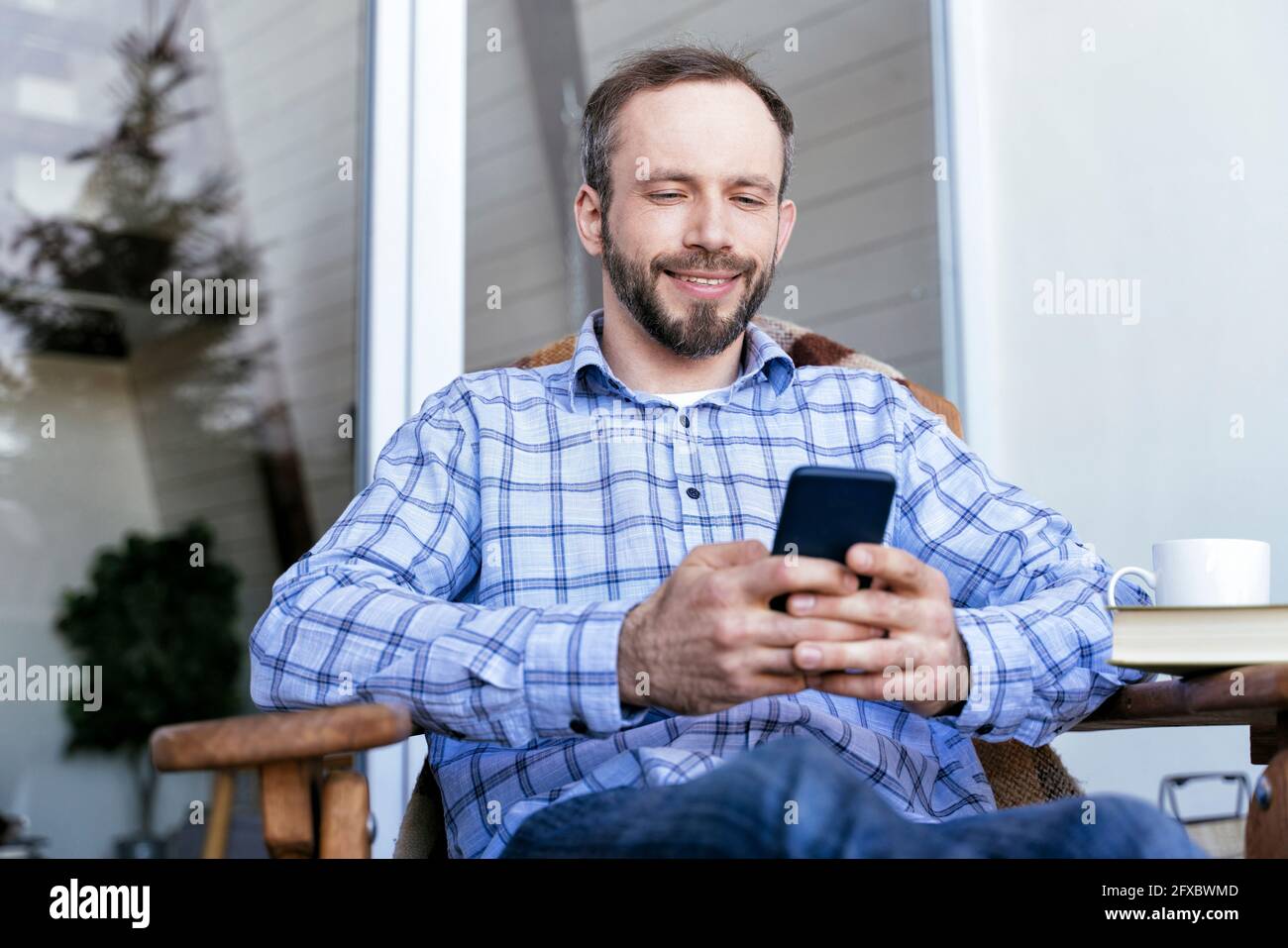 Uomo in abbigliamento casual utilizzando smartphone sul balcone Foto Stock