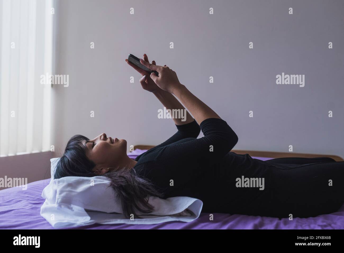 Messaggi di testo di una donna mid adult su smartphone in camera da letto Foto Stock