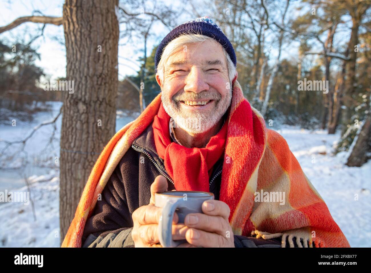 Uomo anziano sorridente in coperta che tiene la tazza di caffè durante l'inverno Foto Stock