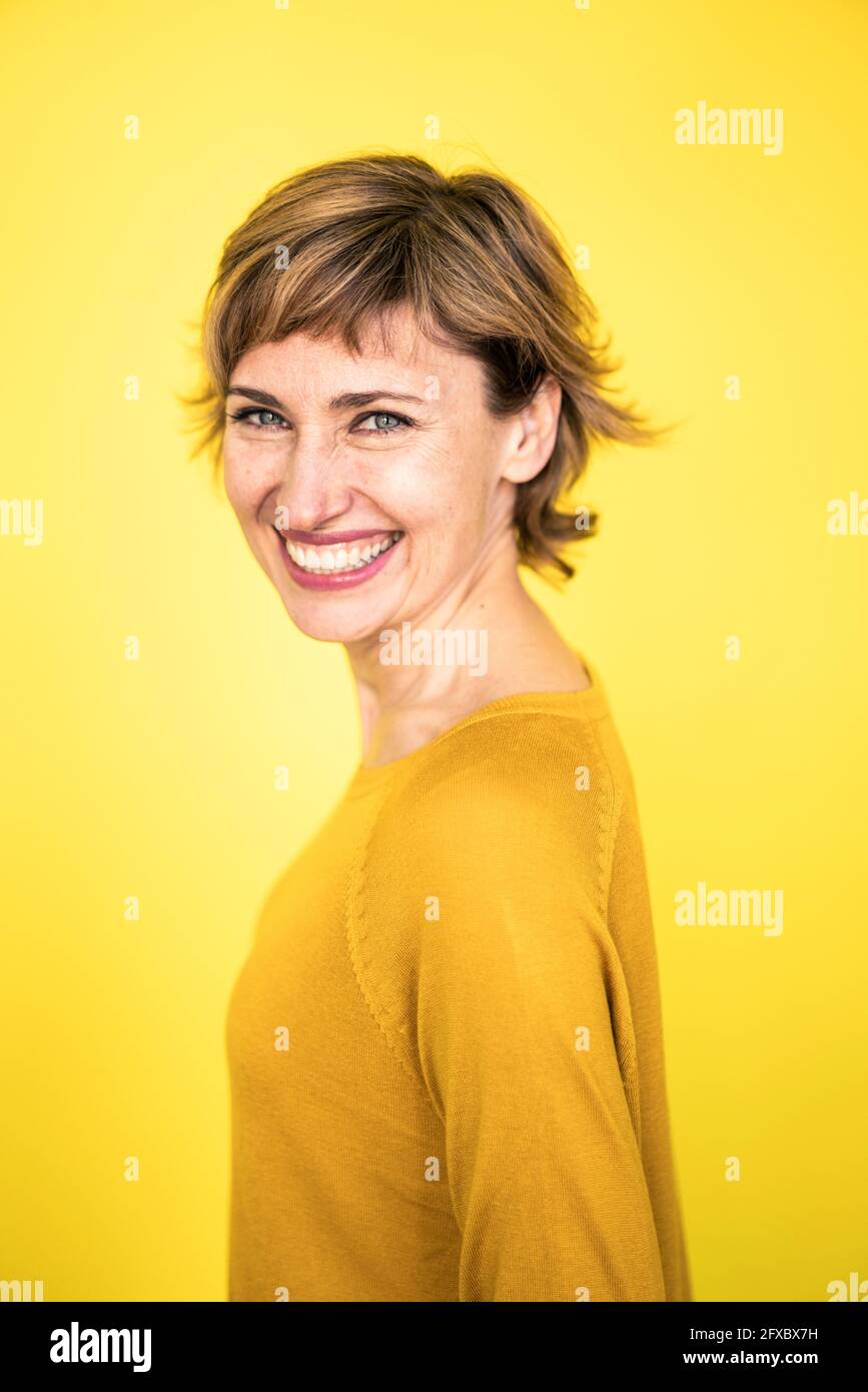 Donna matura allegra in piedi da sfondo giallo Foto Stock