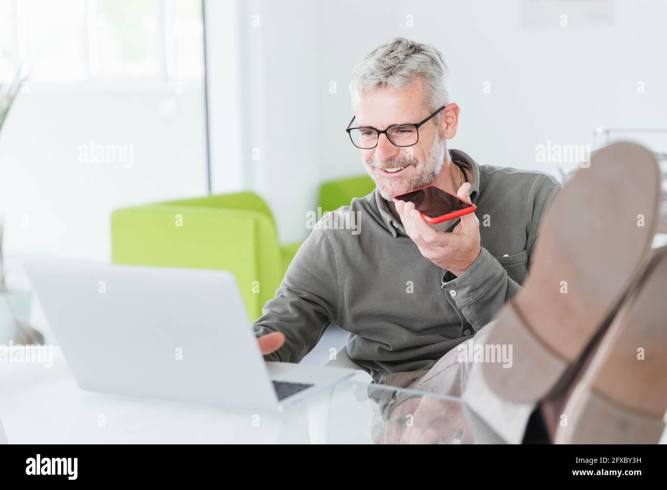 Sorridente uomo d'affari che usa il computer portatile durante l'invio della posta vocale in ufficio Foto Stock