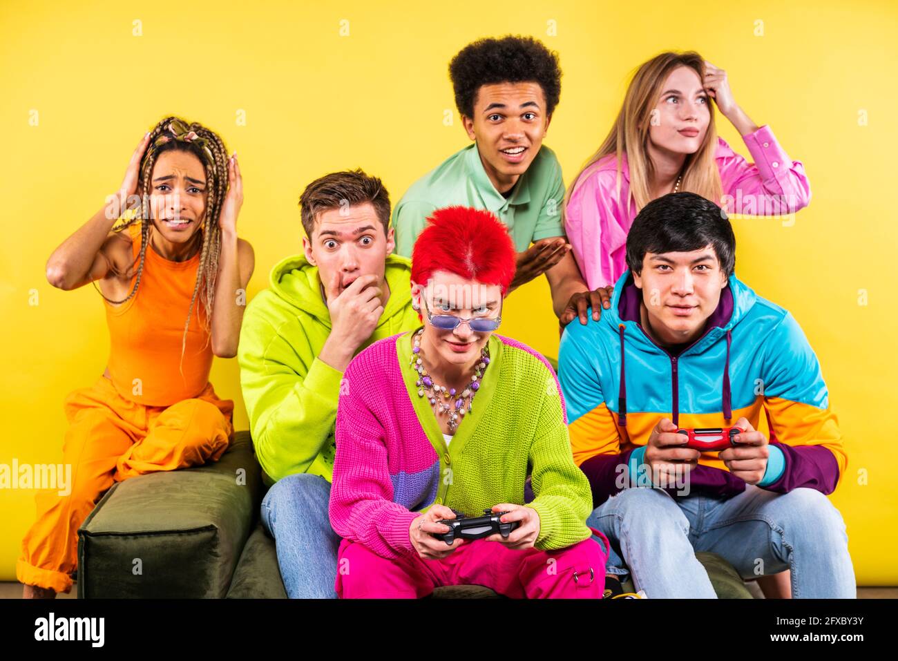 Donne che fanno i volti mentre si siedono con gli amici davanti a sfondo giallo Foto Stock