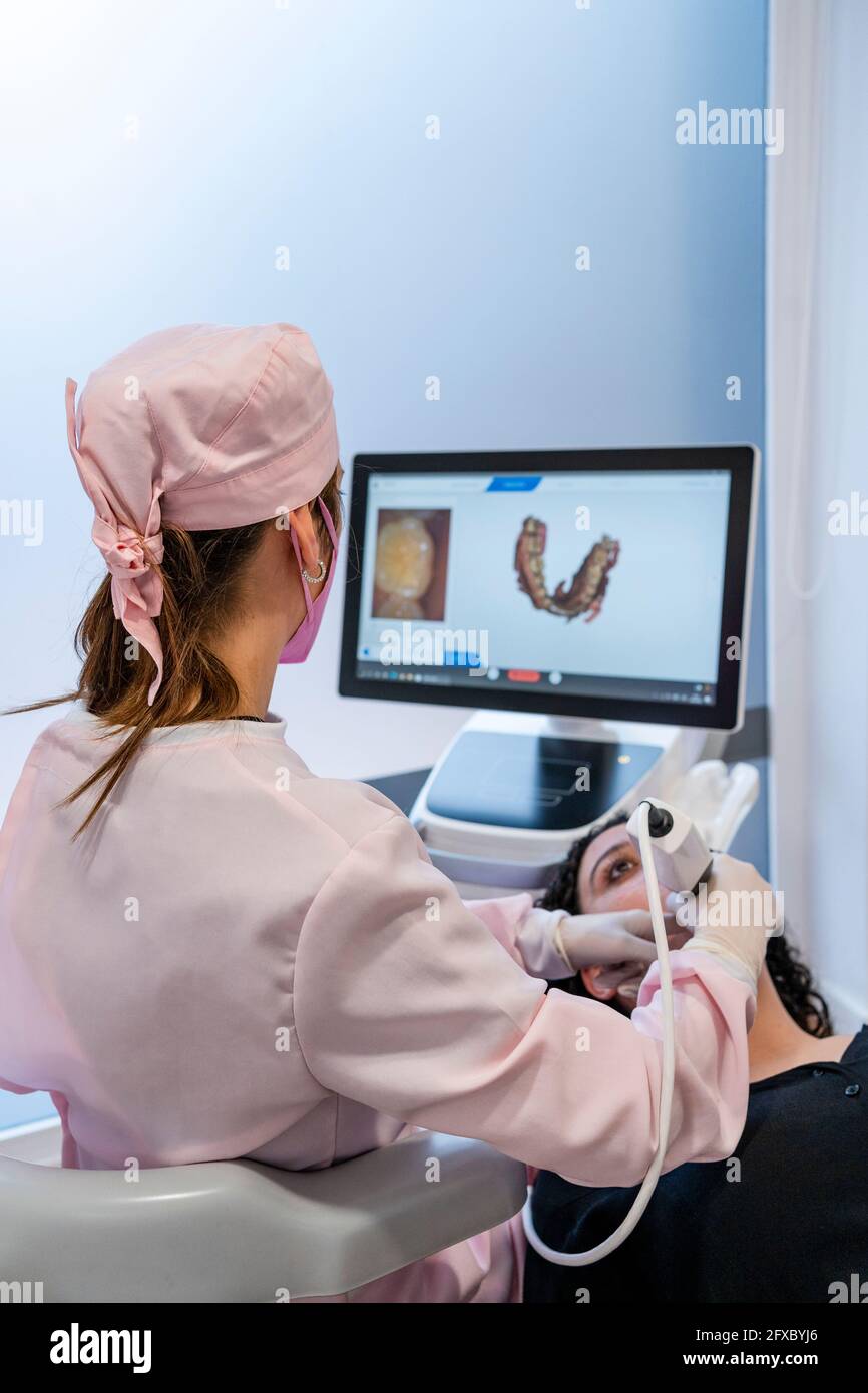 Dentista femminile che controlla i denti del paziente mentre guarda l'immagine digitale sullo schermo della clinica Foto Stock