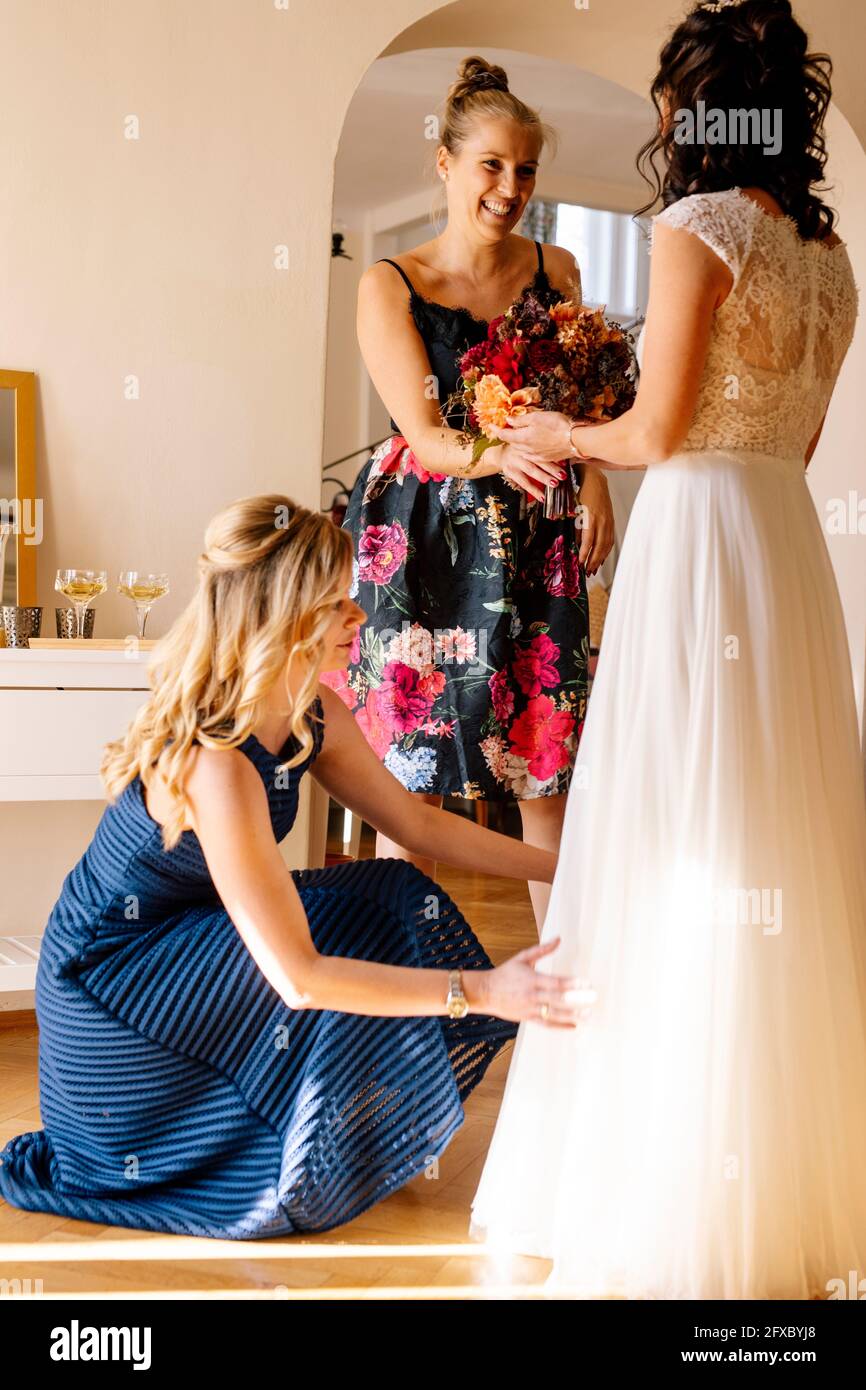Donna sorridente che dà bouquet alla sposa in camera domestica Foto Stock