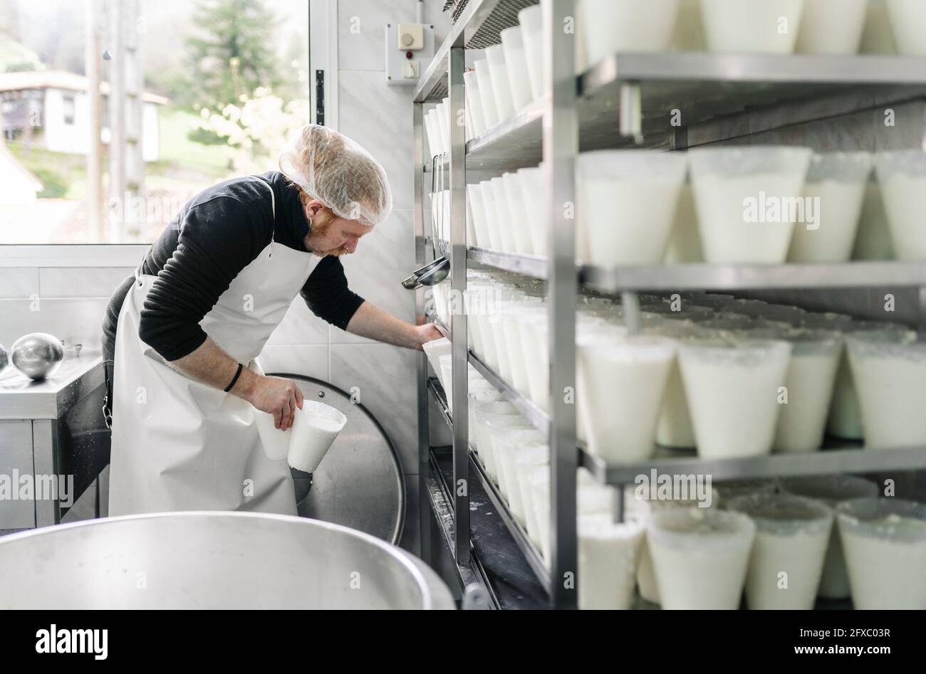 Imprenditore maschio maturo che organizza contenitori di formaggio in rack in deposito Foto Stock