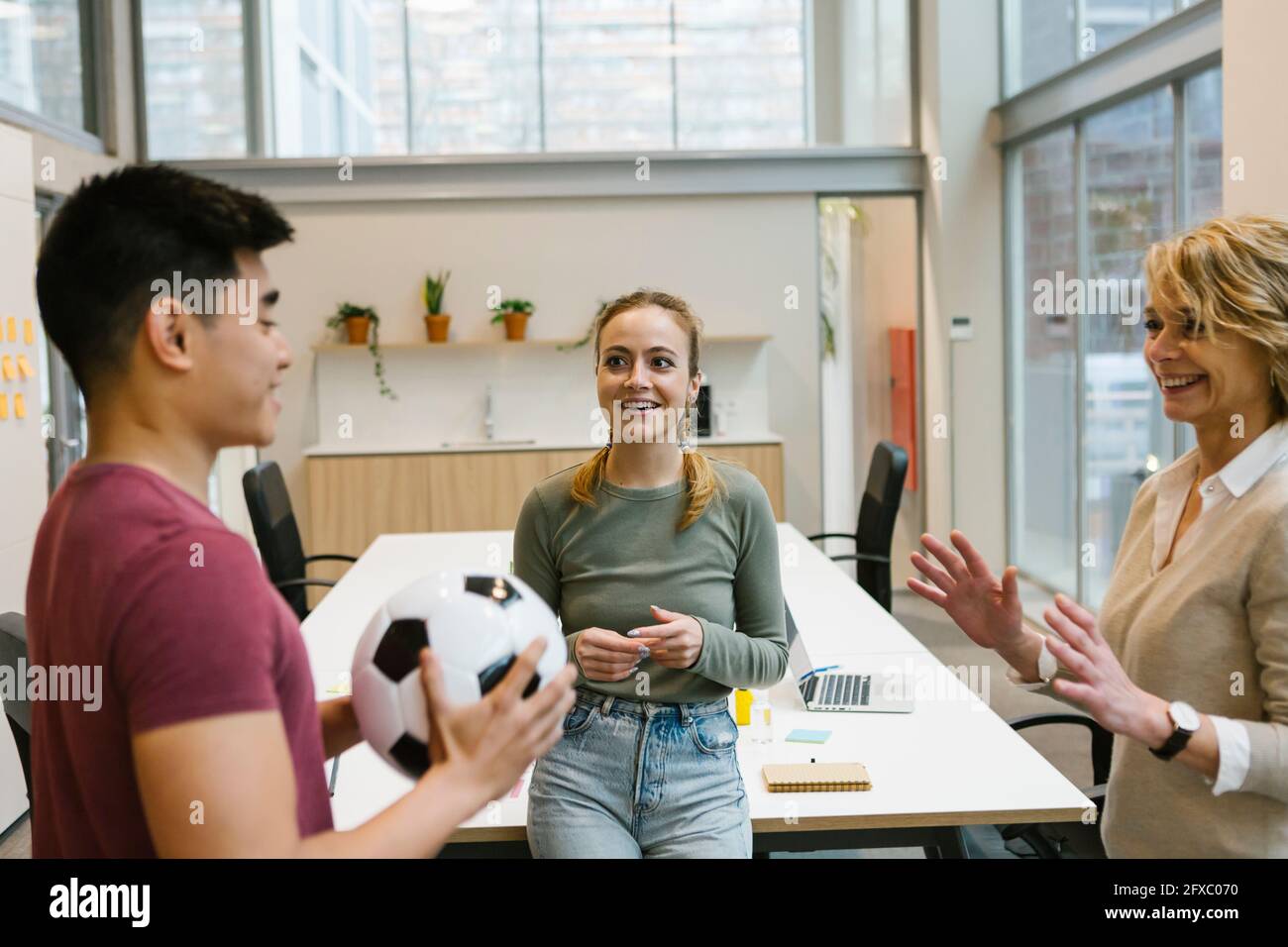 Sorridenti professionisti maschili e femminili che giocano con la palla da calcio presso l'ufficio dei colleghi Foto Stock