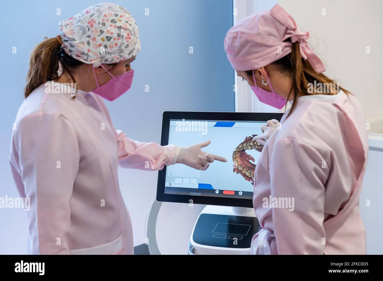 Dentisti femminili in uniforme che esaminano l'immagine digitale dei denti sullo schermo presso la clinica Foto Stock
