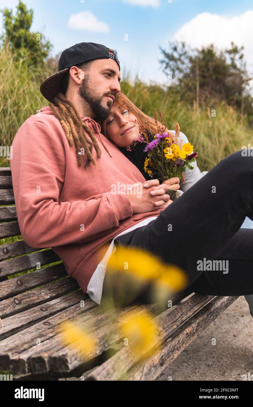 Giovane donna che si rilassa sulla spalla del ragazzo sulla panchina Foto Stock