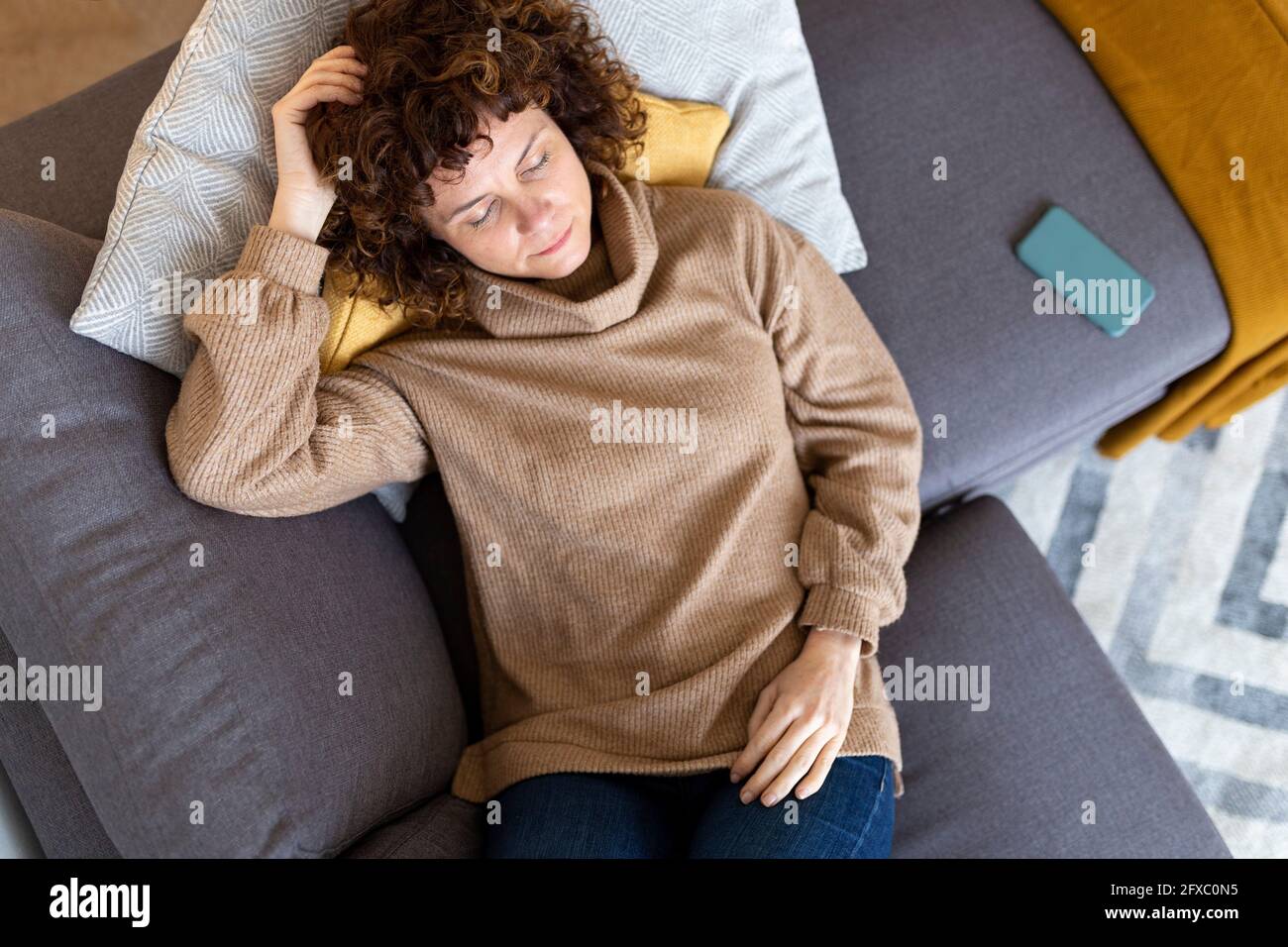 Donna che si rilassa dal telefono cellulare sul divano nel soggiorno di casa Foto Stock