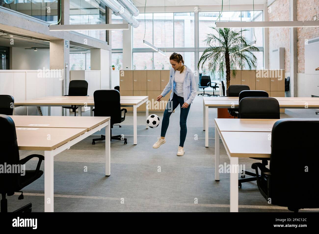 Donna d'affari che gioca con la palla di calcio presso l'ufficio di coworking Foto Stock