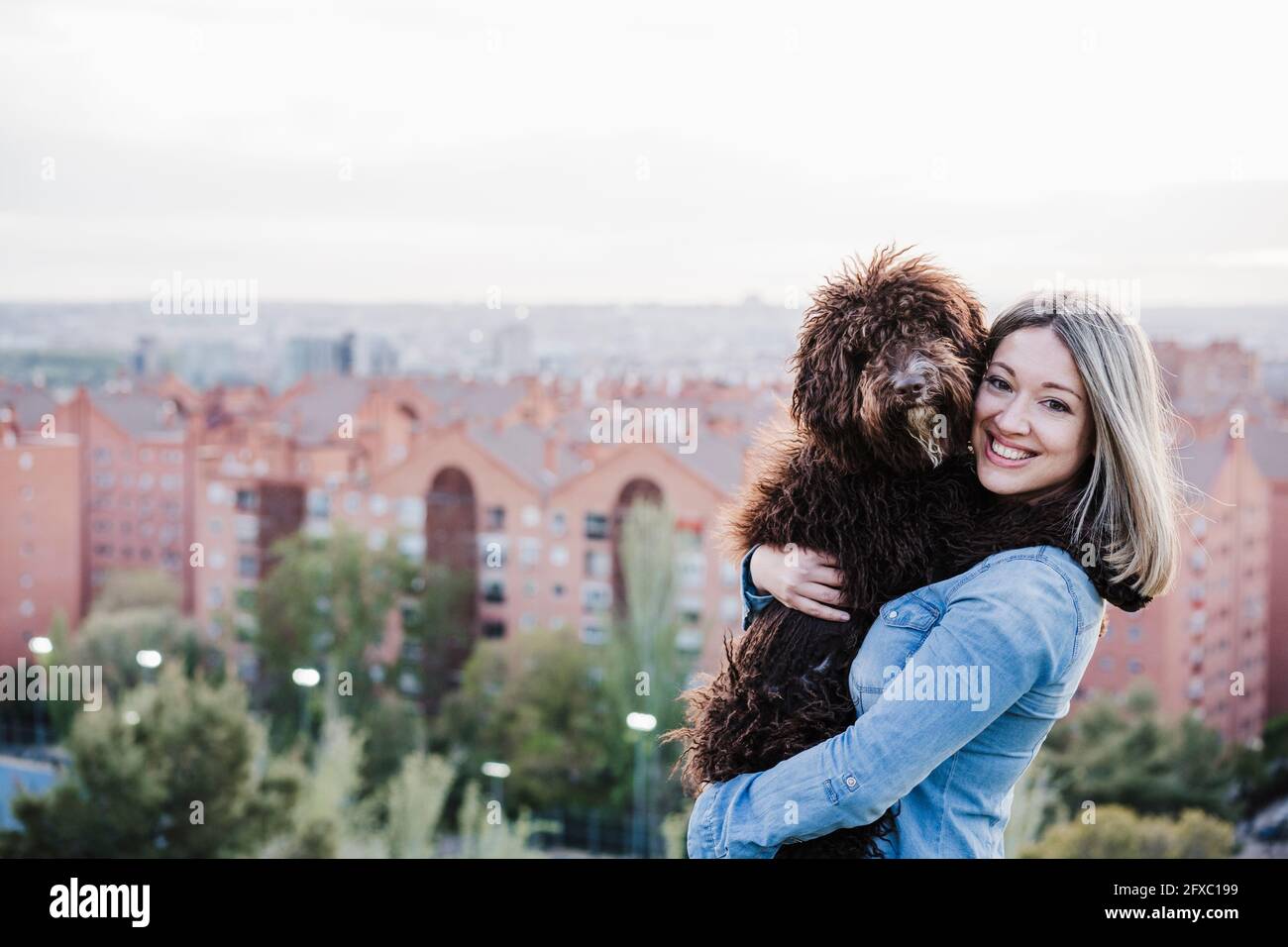 Felice bella donna che porta il cane dal paesaggio urbano Foto Stock