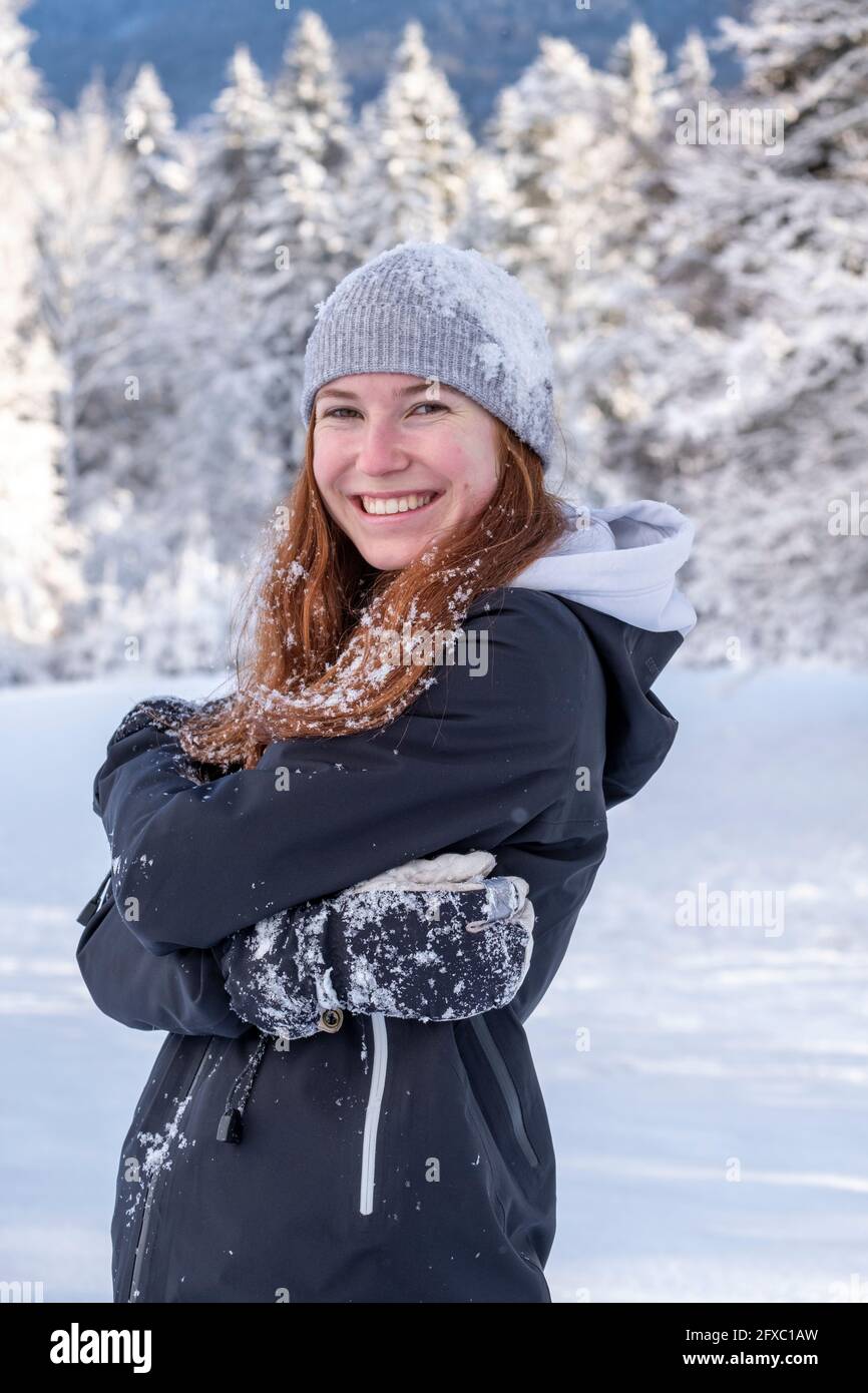 Donna felice in maglia cappello sorridente mentre in piedi su terra coperta di neve durante l'inverno Foto Stock