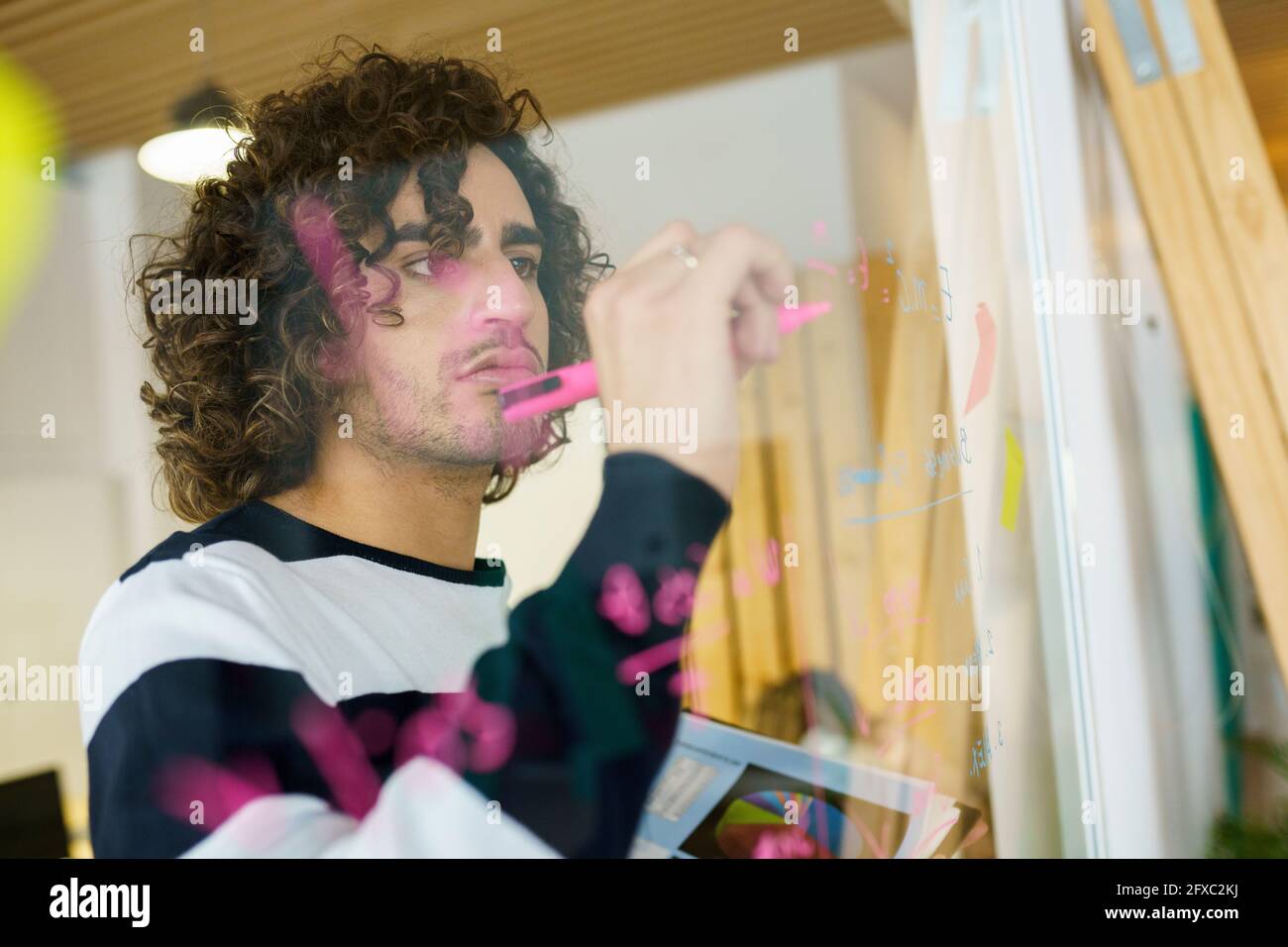 Un uomo d'affari creativo che scrive su una parete di vetro in ufficio Foto Stock