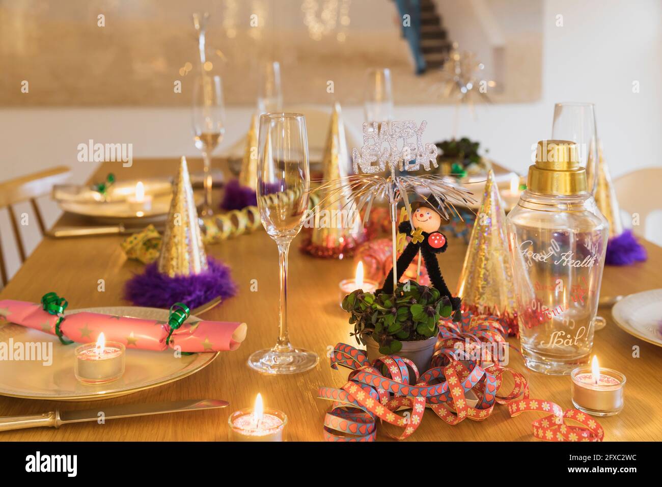 Tavolo festivo della vigilia di Capodanno con piatti, candele, cappelli da festa, flauti di champagne e figurine spazzamento camino Foto Stock
