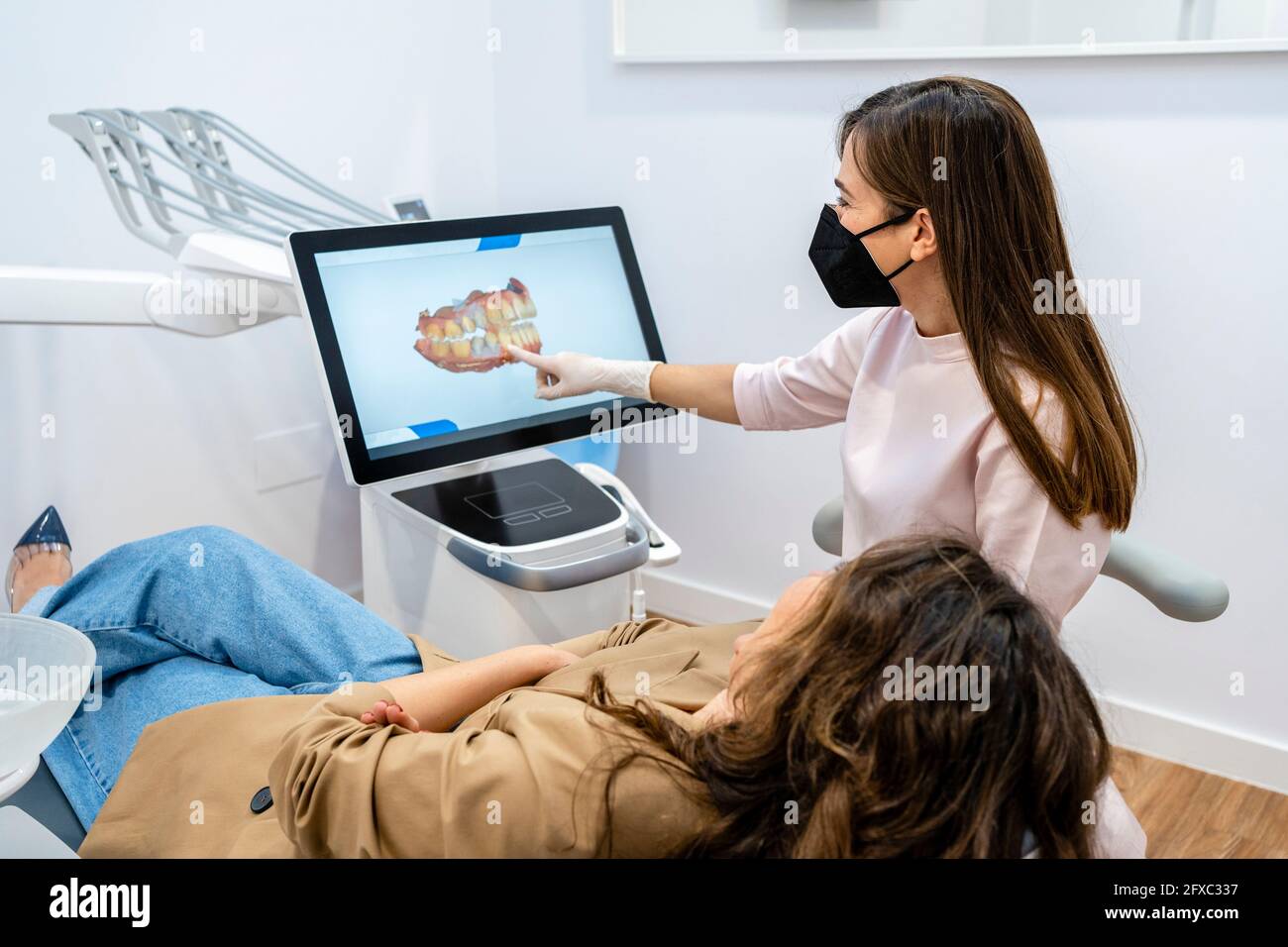 Dentista femminile che spiega sullo schermo del computer al paziente in clinica durante la pandemia Foto Stock