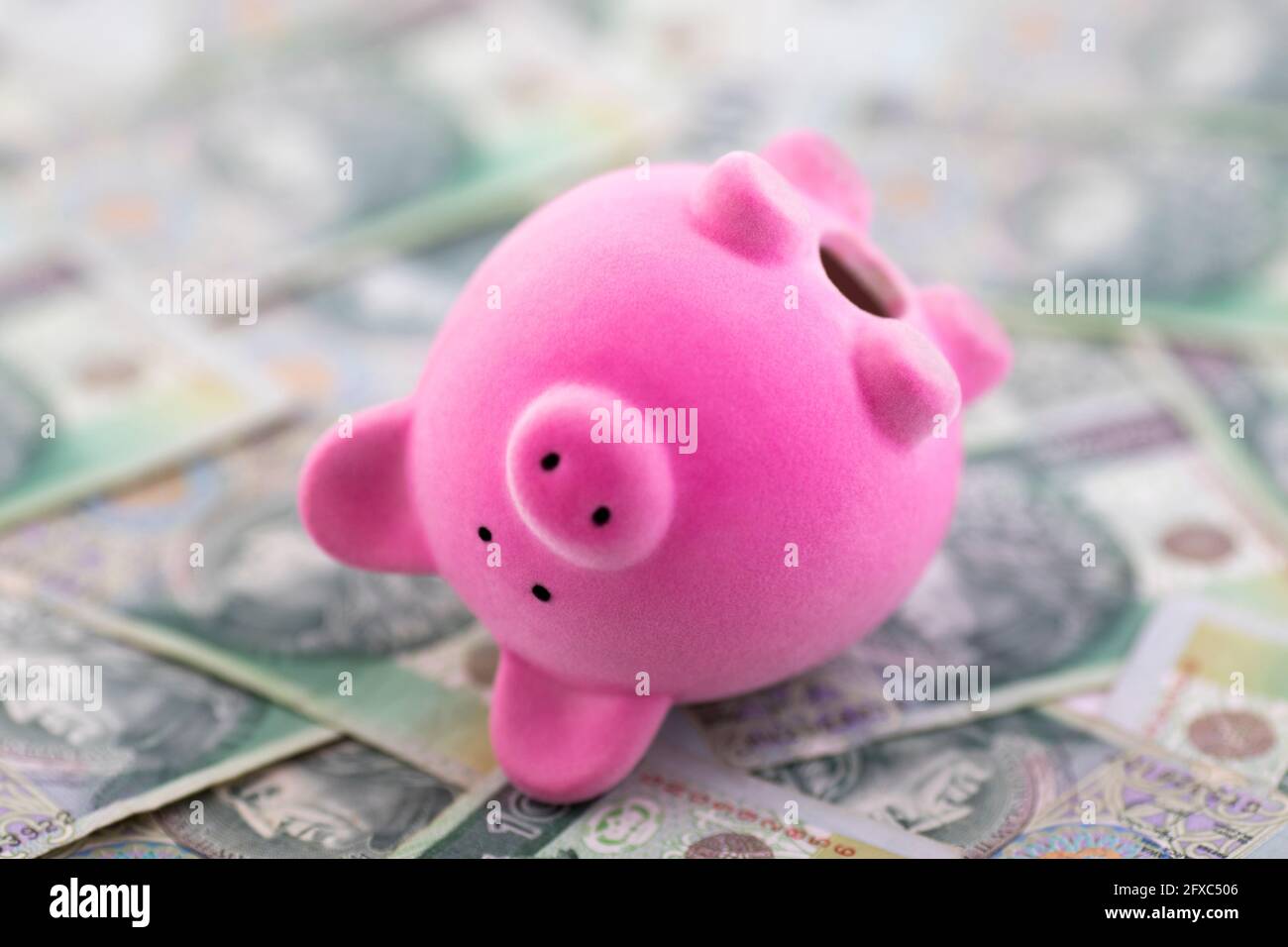 Pink piggy banca capovolta su soldi lucidati Foto Stock