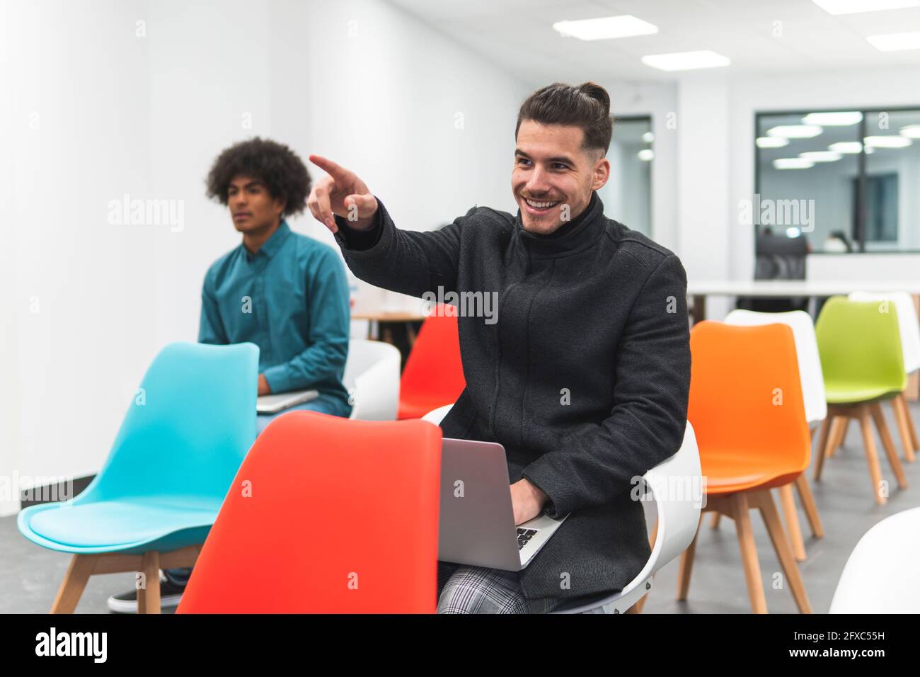Uomo d'affari sorridente gesturing mentre si siede da collaboratore in classe Foto Stock