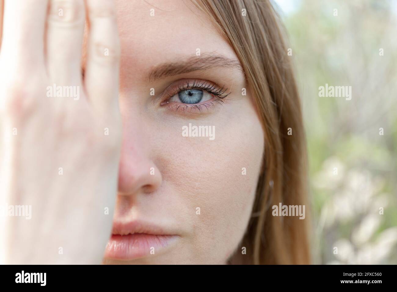 Giovane donna fissando mentre coprendo il viso con la mano Foto Stock