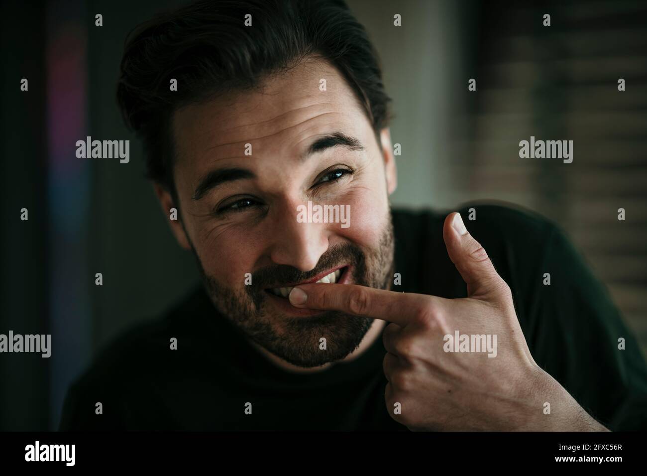 Uomo sorridente che tocca i denti con il dito indice Foto Stock