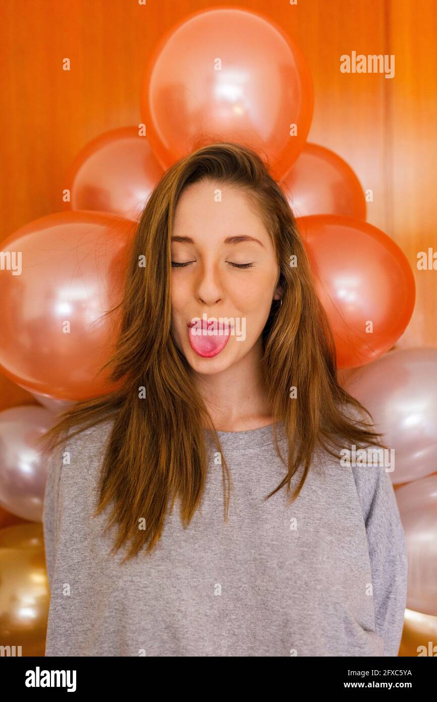 Donna con gli occhi chiusi attaccando la lingua da palloncini decorazione a casa Foto Stock