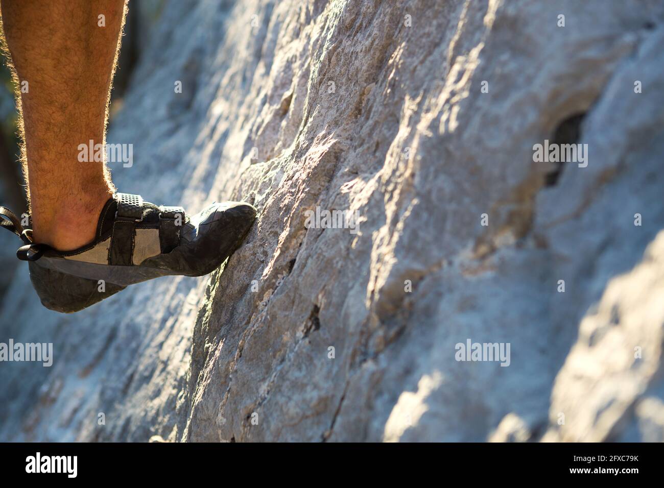 Le scarpe da arrampicata sui piedi dell'arrampicatore appoggiano la punta sulla roccia. Sport estremi, turismo di montagna. Primo piano. Spazio di copia. Gamba maschio pelosa Foto Stock