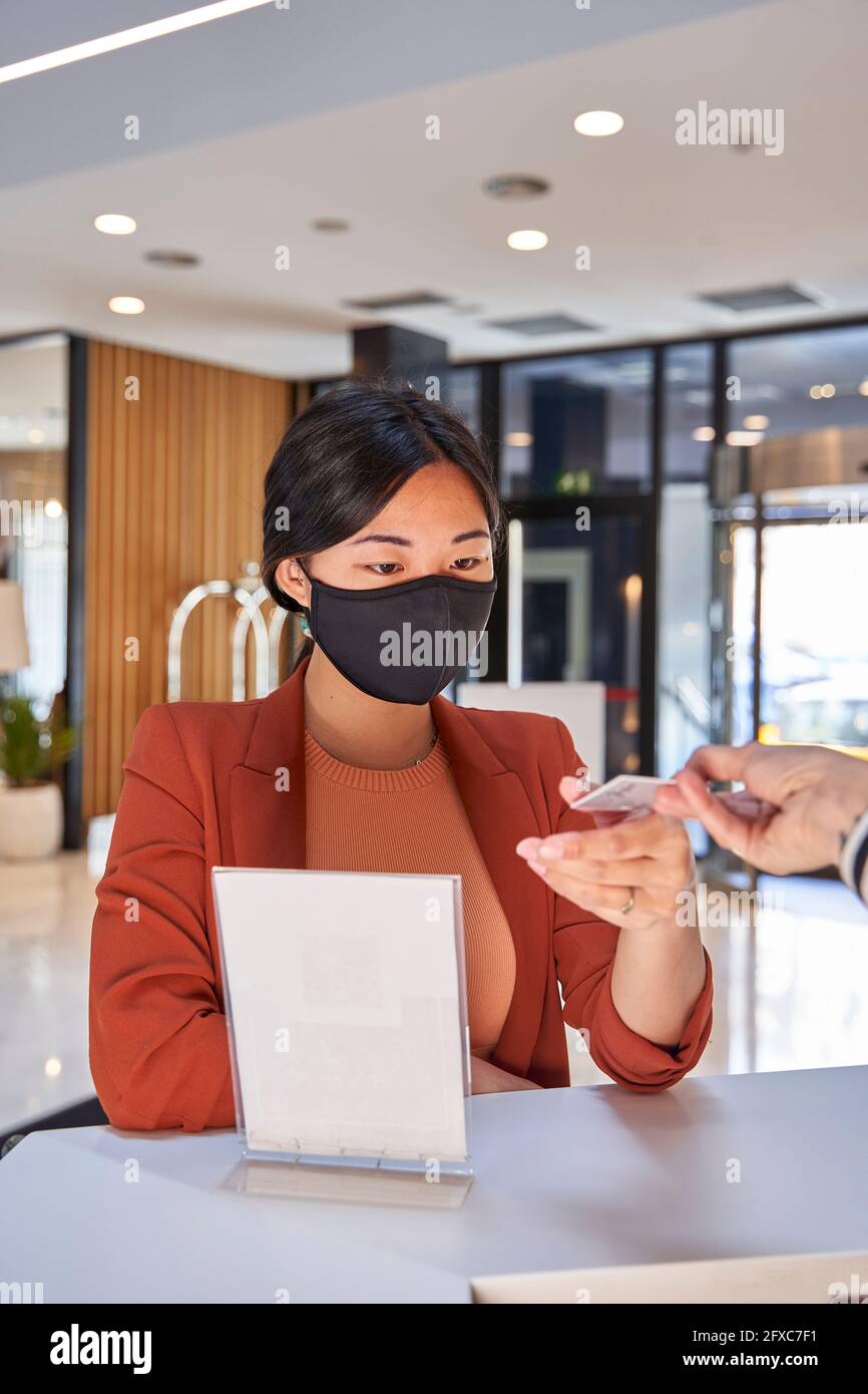 Donna che indossa la maschera facciale che prende la chiave di carta dall'addetto alla reception dell'hotel Foto Stock