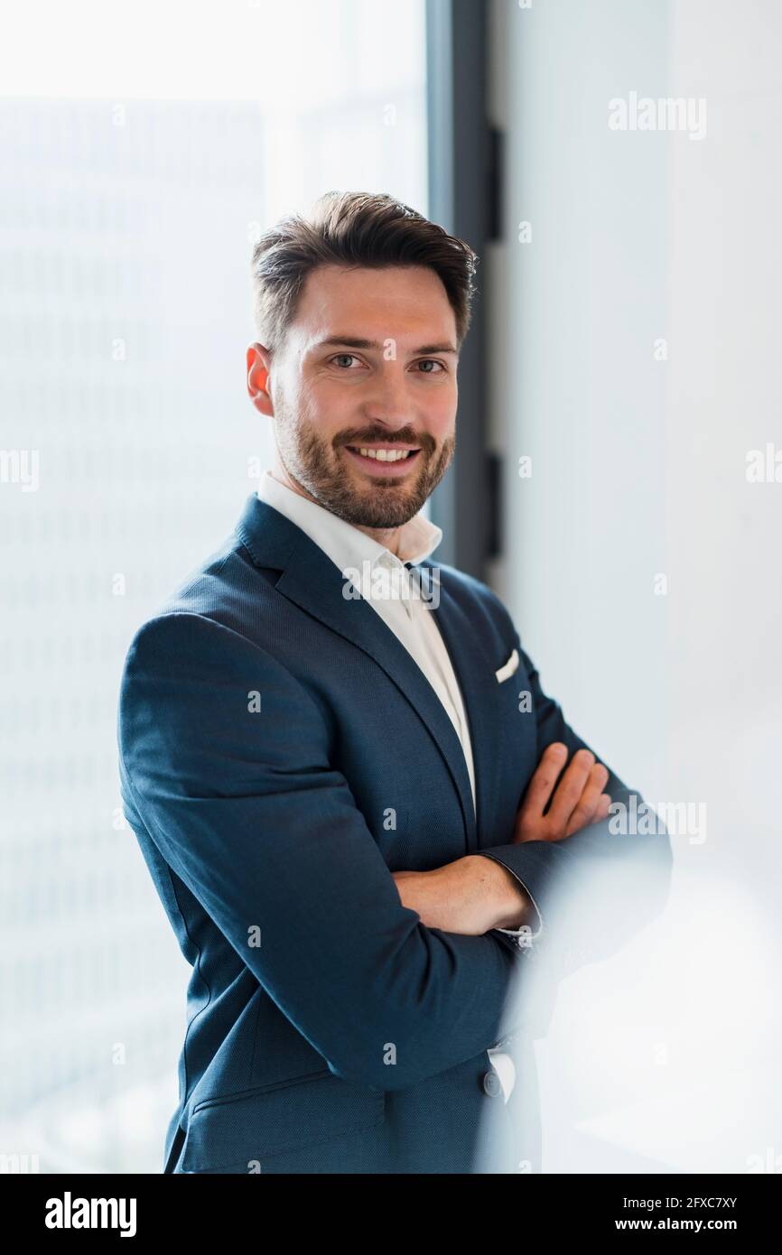 Sorridente imprenditore maschio con braccia incrociate sul posto di lavoro Foto Stock