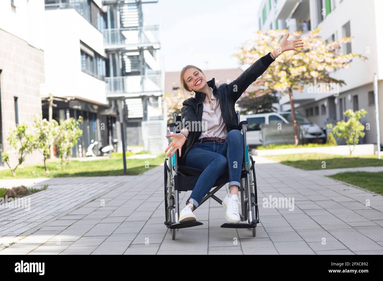 Felice donna disabile con braccia distese seduta su sedia a rotelle in zona residenziale Foto Stock