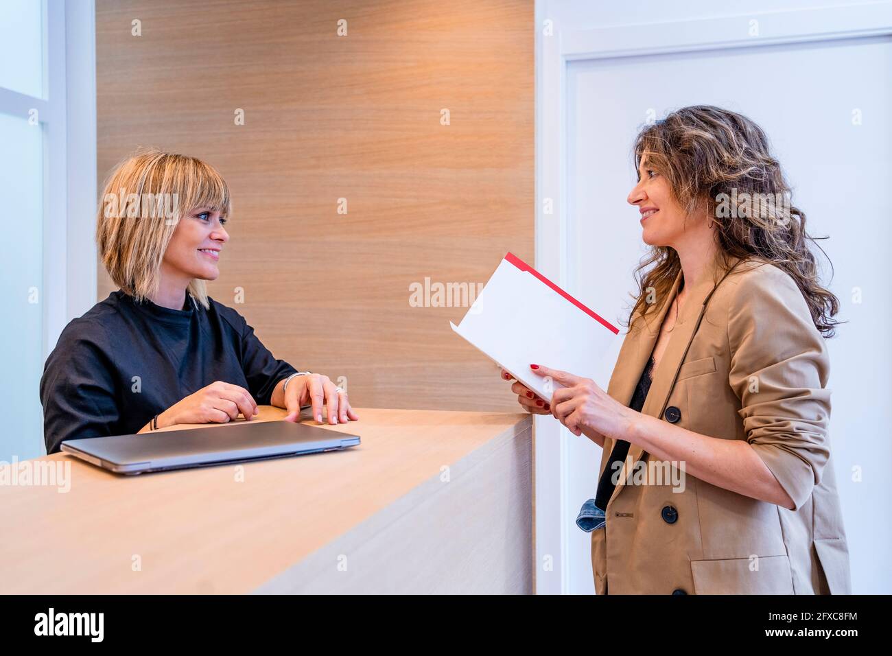 Sorridente receptionist femminile che guarda il rapporto di attesa del paziente in clinica Foto Stock